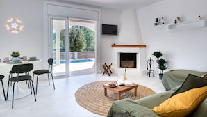 A modern living room with a fireplace, a dining area with chairs and a table, and a view of the outdoors.