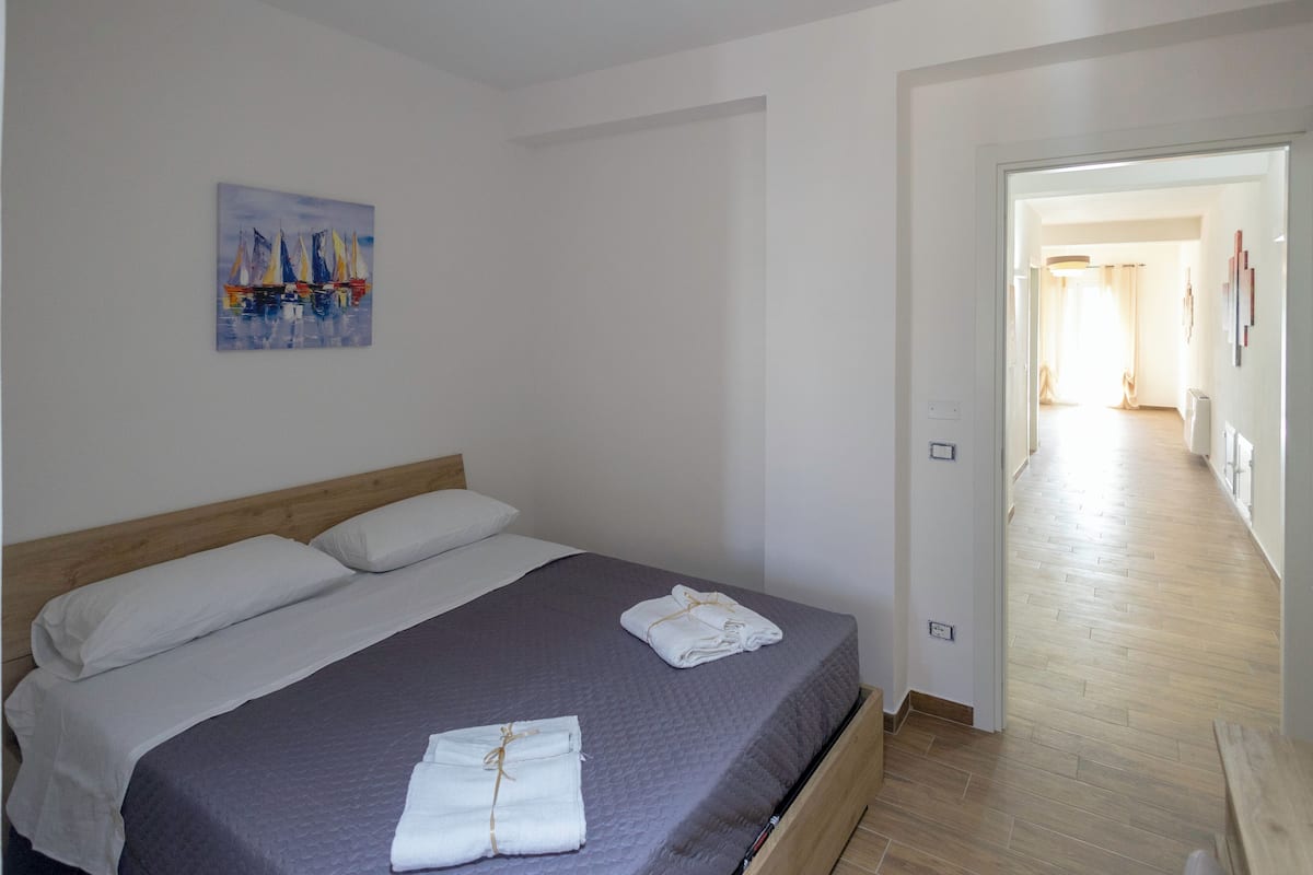 A neatly made bed with white linens and towels, a painting on the wall, and a wooden floor.