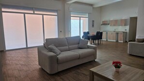A spacious living area with a sofa, a dining table, and a kitchen in the background. - ELYSIUM (Mazara del Vallo)