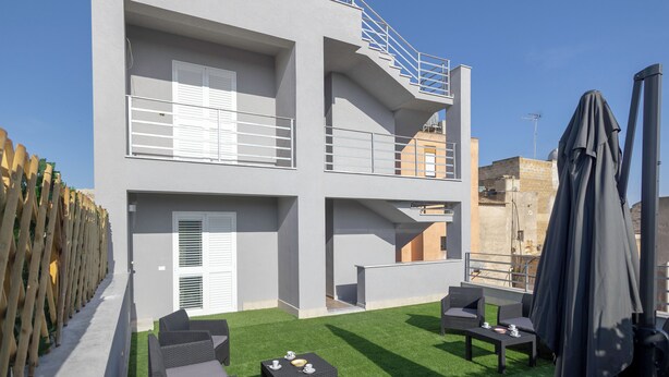 A modern building with a balcony, outdoor seating, and a covered area. - ELYSIUM (Mazara del Vallo)