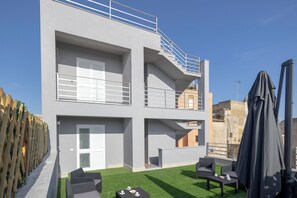 A modern building with a balcony, outdoor seating, and a covered area. - ELYSIUM (Mazara del Vallo)
