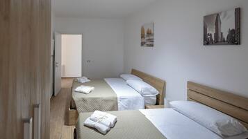 A hotel room with two beds, a wooden door, and a cityscape painting on the wall.