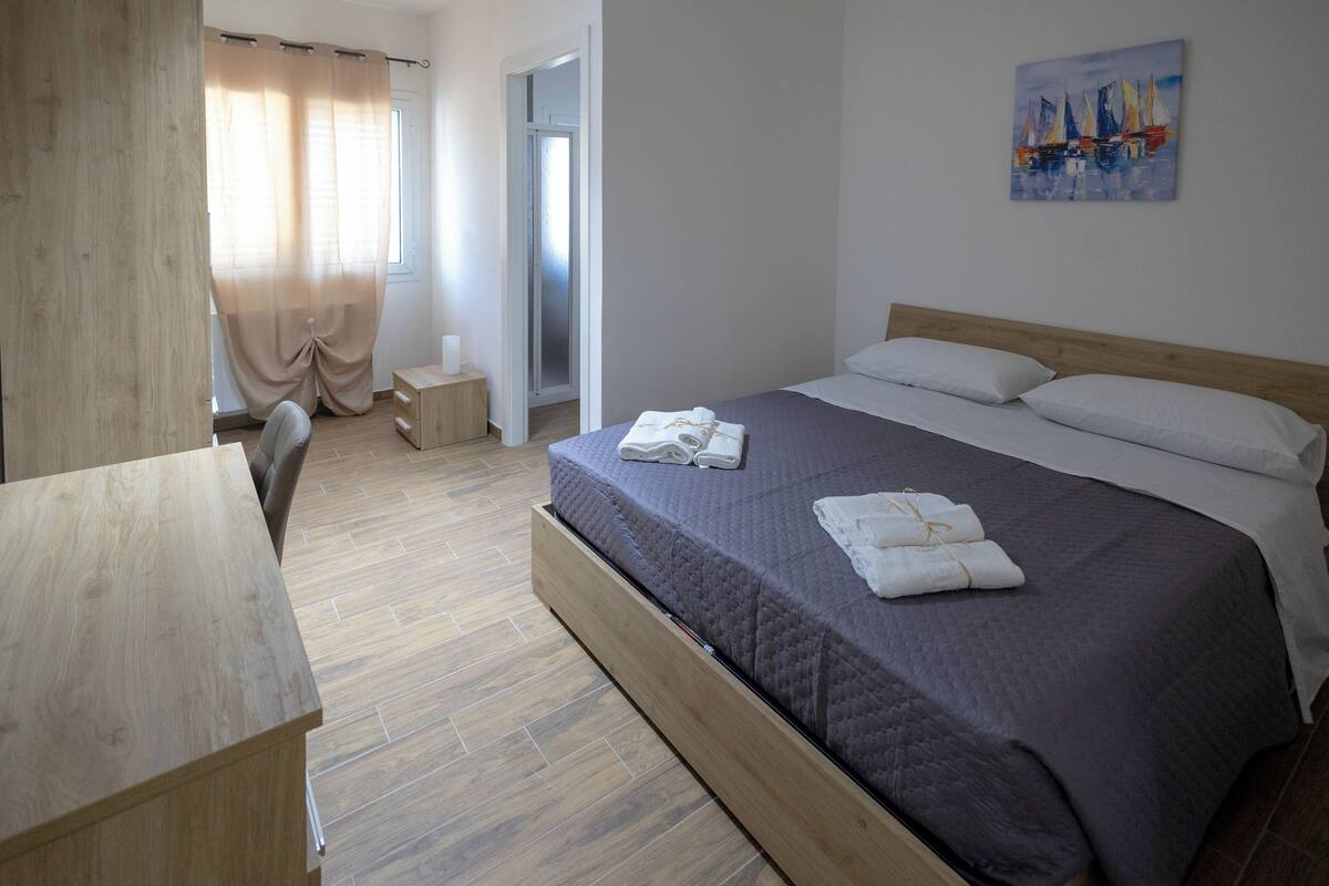 A hotel room with a wooden bed, a desk, a chair, and a window with curtains.