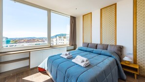 A bedroom with a large window, a bed with blue bedding, a nightstand, and a view of the cityscape. - Chiave di Fuga - Doppia Deluxe (Naples)