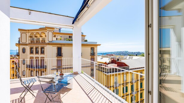 A balcony with a table and chairs, a view of a yellow building, and a clear sky. - Chiave di Fuga - Doppia Deluxe (Naples)