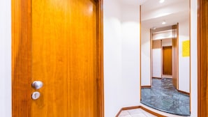 Un pasillo con puerta de madera, suelo de baldosas y pared espejada.