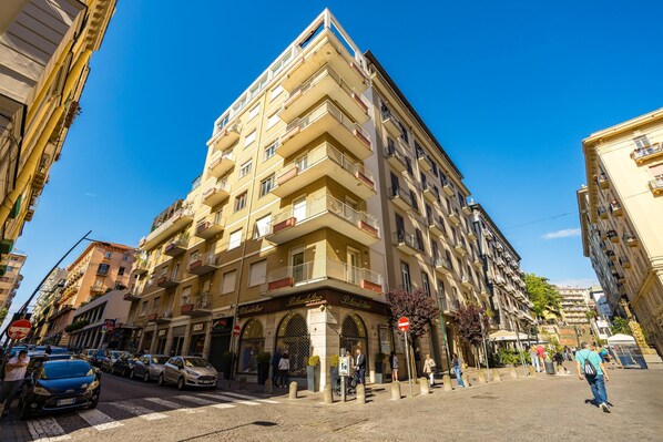 A multi-story building with balconies, a ground-floor entrance, and a clear blue sky.