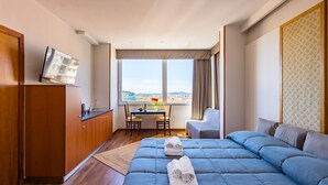 A hotel room with a large bed, a desk with two chairs, a TV on the wall, and a view of the city through the window. - Chiave di Fuga - Tripla Superior (Naples)