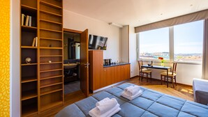 A hotel room with a bed, a wooden wardrobe, a desk with a chair, and a large window offering a city view. - Chiave di Fuga - Tripla Superior (Naples)