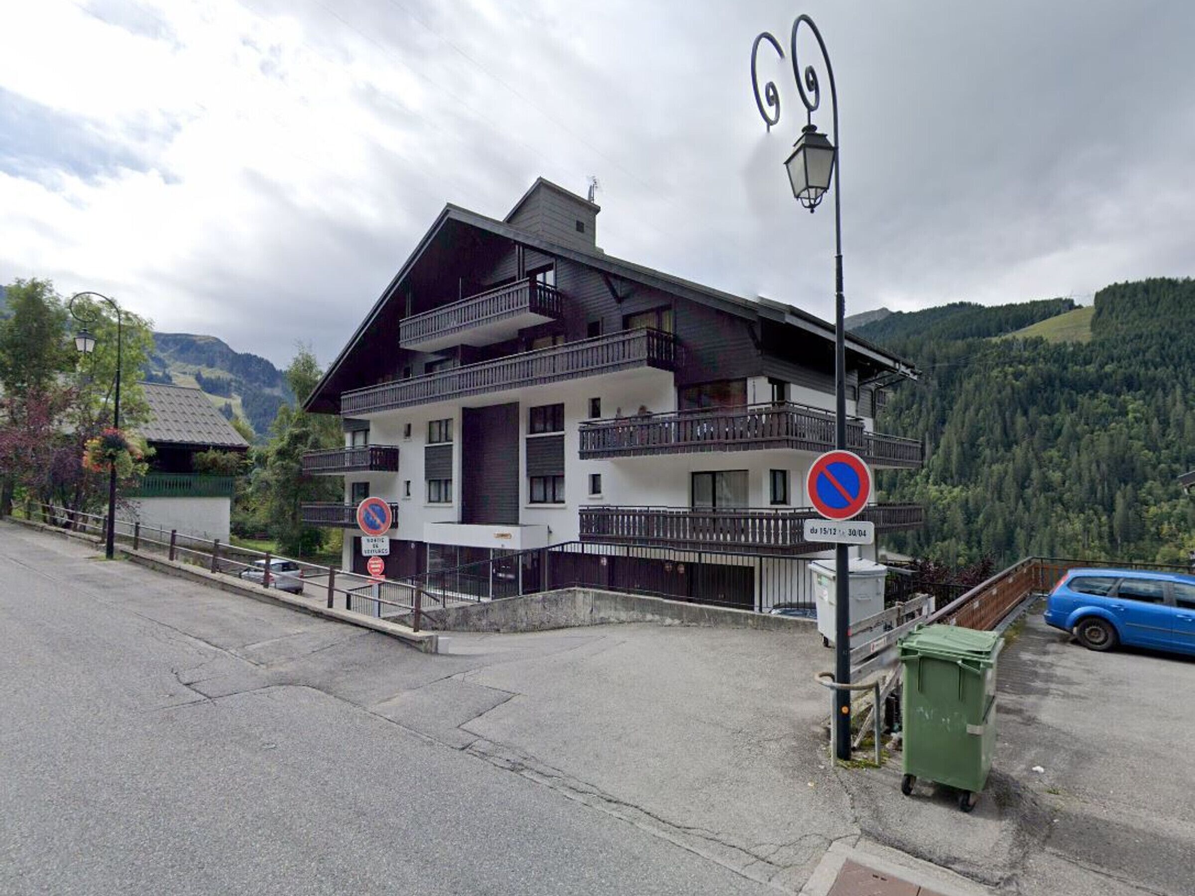Un immeuble à deux étages doté de balcons, d’un panneau indiquant qu’il est interdit de se garer et ayant une chaîne de montagnes en arrière-plan.