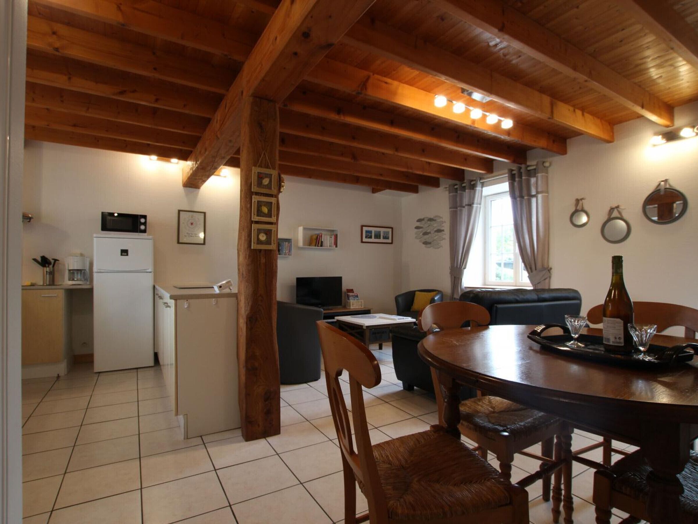 Una cocina acogedora con refrigerador, microondas y vigas de madera. Hay una mesa de comedor con sillas y un sofá en la sala.