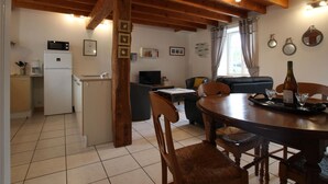 Eine gemütliche Küche mit Kühlschrank, Mikrowelle und Holzbalken. Im Wohnbereich befindet sich ein Esstisch mit Stühlen sowie eine Couch.