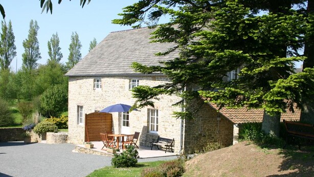 Ein Steinhaus mit Ziegeldach, einer Holztür und einer Terrasse mit Tisch und Stühlen.