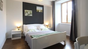 A bedroom with a bed, bedside tables, a hanging light, a window with curtains, and artwork on the wall. - Charming house in Vessey with TV and internet (Pontorson)