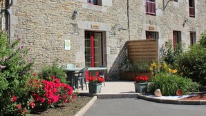 A stone building with a red door labeled "La Cave," outdoor seating, and potted plants. - Charming house in Vessey with TV and internet (Pontorson)