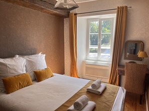 Ein Hotelzimmer mit einem großen Bett, einem Sessel, einem Fenster mit Vorhängen und einem Spiegel.
