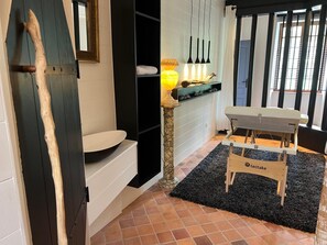 A bathroom with a wooden door, a white sink, a black rug, and a wooden bench.
