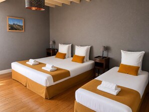 A hotel room with two beds, each with white linens and orange pillows, a wooden floor, a picture on the wall, and a lamp on the nightstand.
