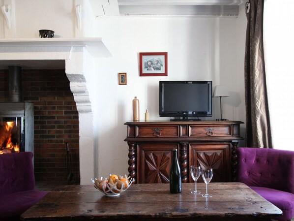 Una sala de estar acogedora con chimenea, televisor, aparador de madera y una mesa con un cuenco de fruta y vasos.
