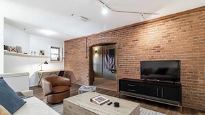 Ein Wohnzimmer mit Backsteinwand, Fernseher, Ledersessel und Sofa.