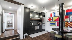 Eine moderne Küche mit dunklen Schränken, einem eingebauten Ofen und einem Edelstahlkühlschrank. Im Essbereich stehen Hocker und ein kleiner Tisch.