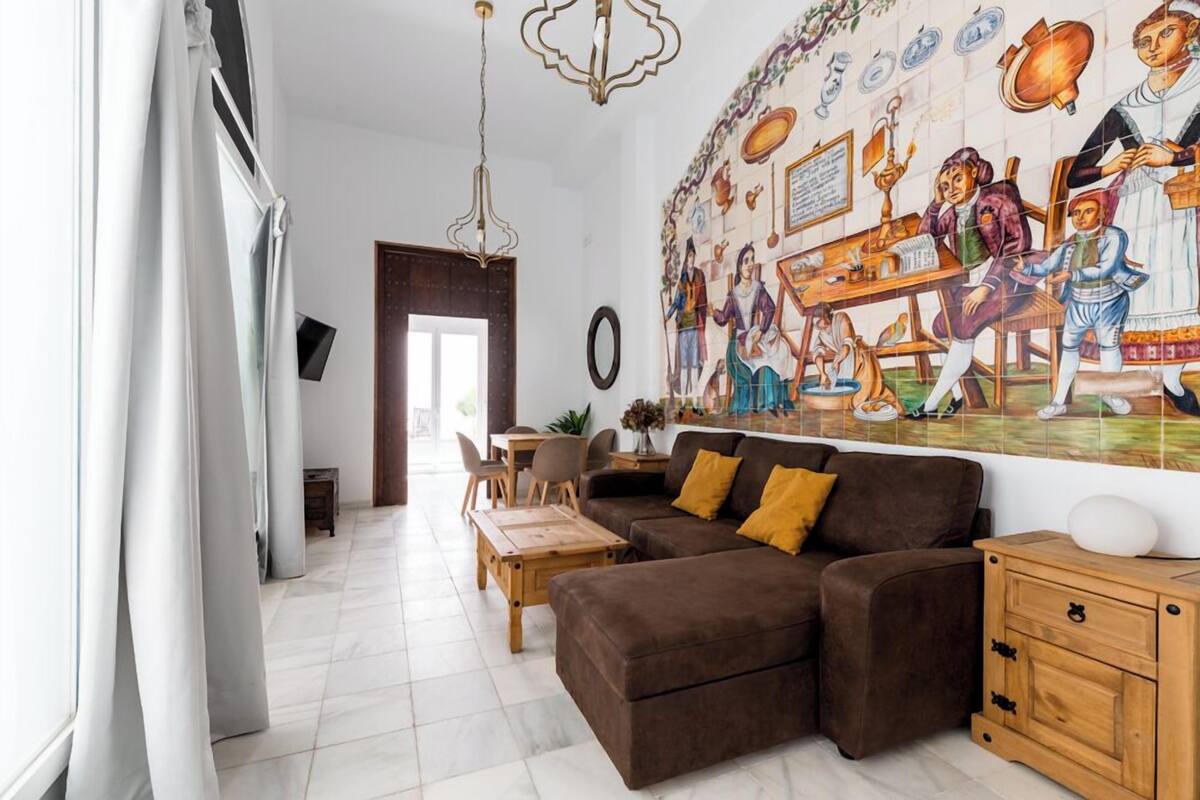 A living room with a brown sofa, a wooden coffee table, and a mural on the wall depicting historical figures.