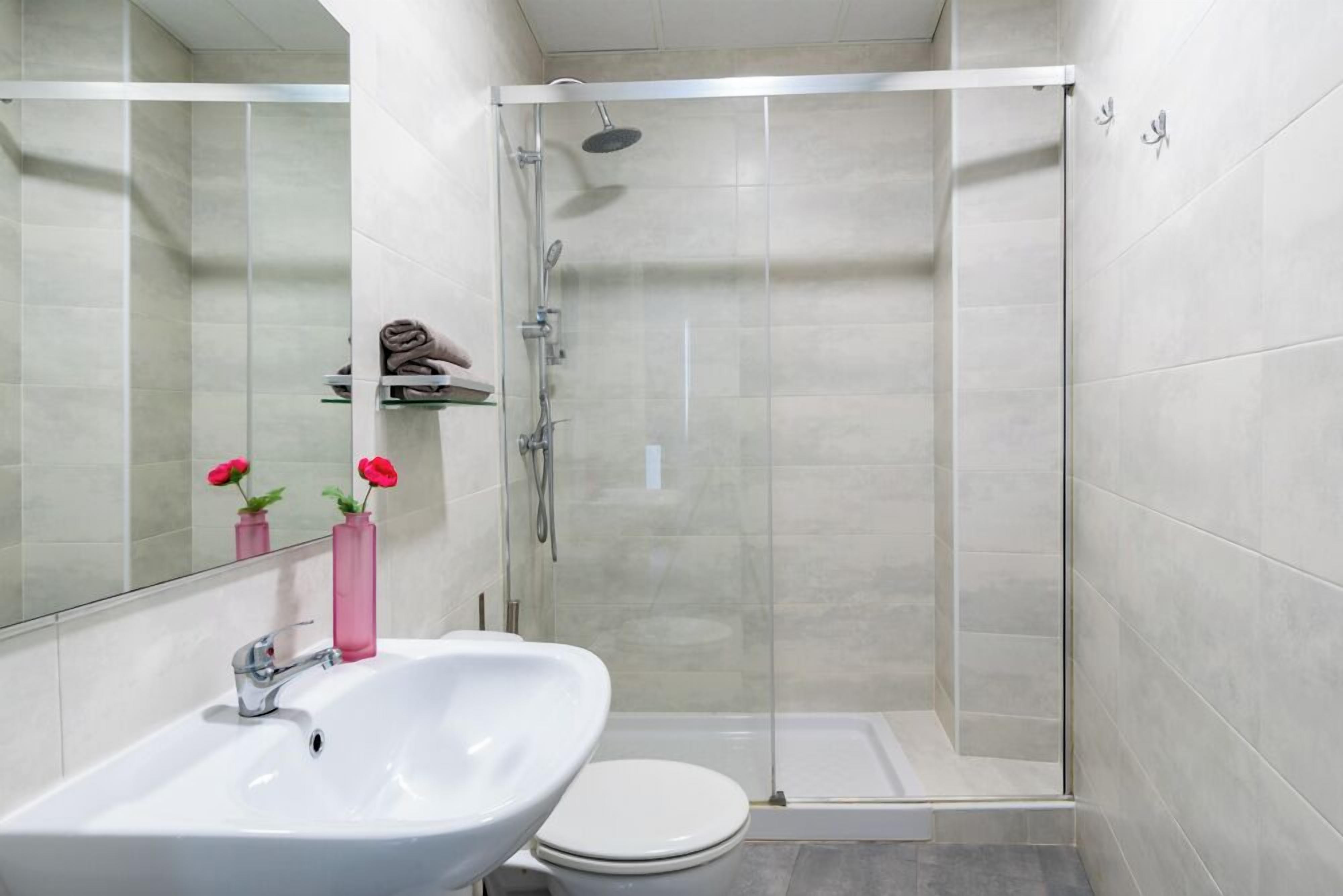 A modern bathroom with a white sink, toilet, and glass-enclosed shower.