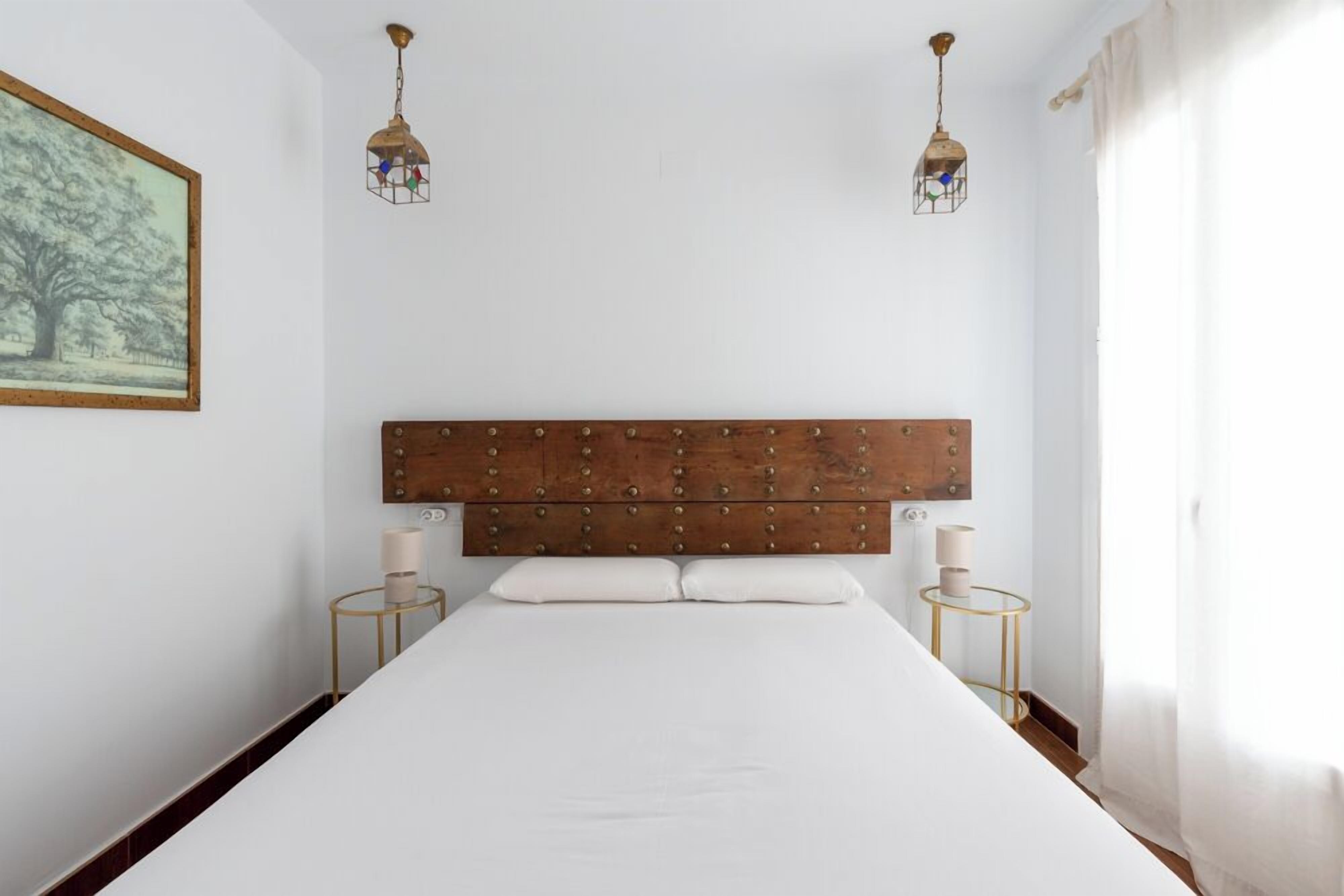 A bedroom with a large bed, two bedside tables, a wooden headboard, and a framed picture on the wall.