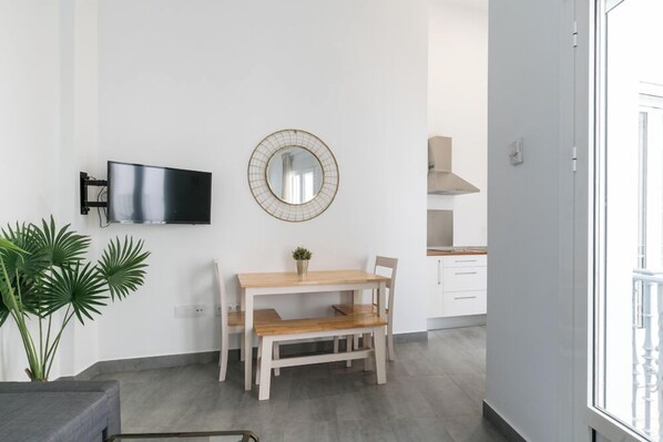 Una sala de estar moderna con una mesa de comedor de madera, un televisor montado en la pared y un espejo redondo.
