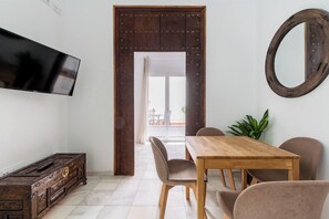 Un coin repas avec une table et des chaises en bois, un téléviseur fixé au mur et un grand miroir.