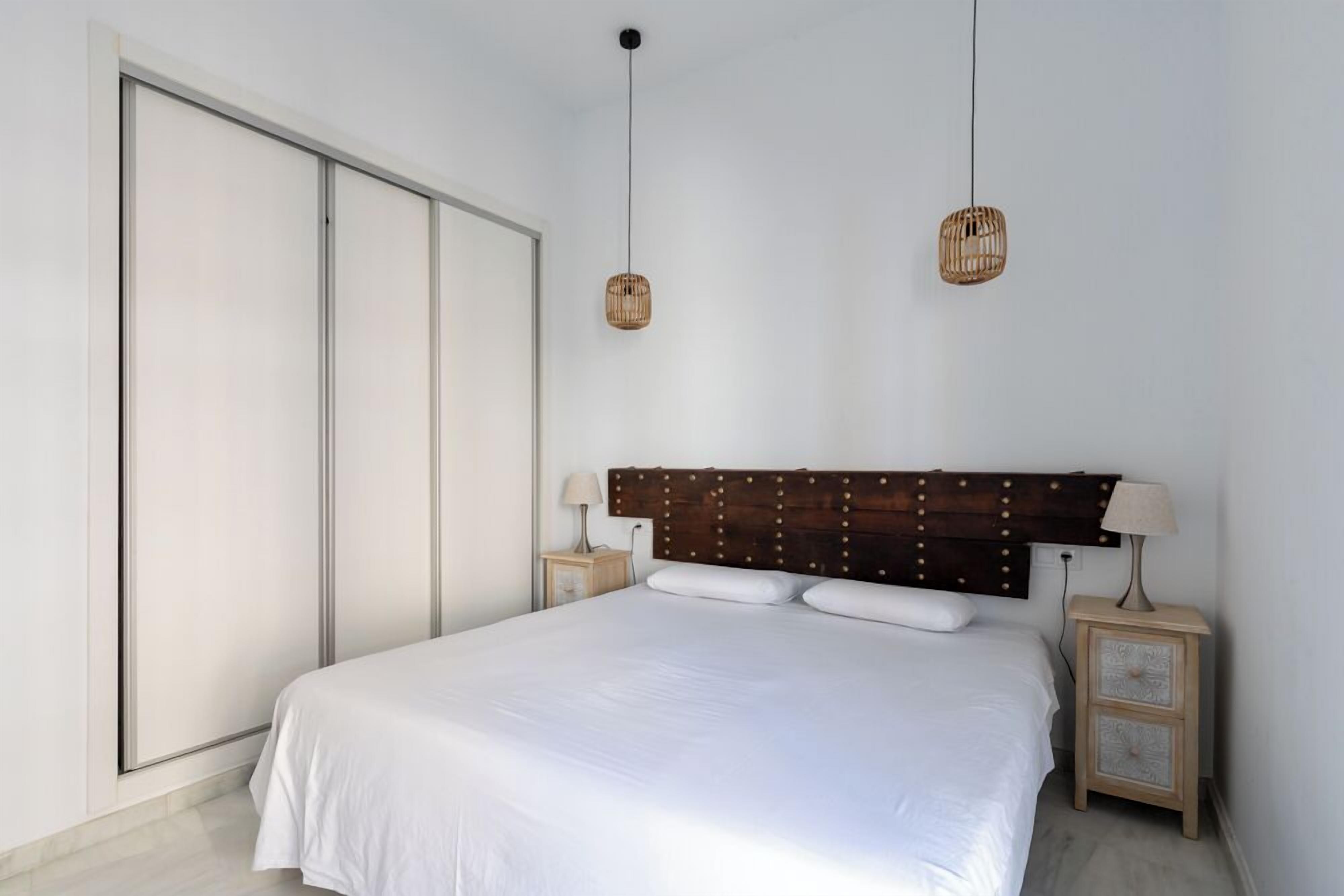 Un dormitorio con una cama grande, un cabecero de madera, dos mesitas de noche con lámparas y una puerta corredera.