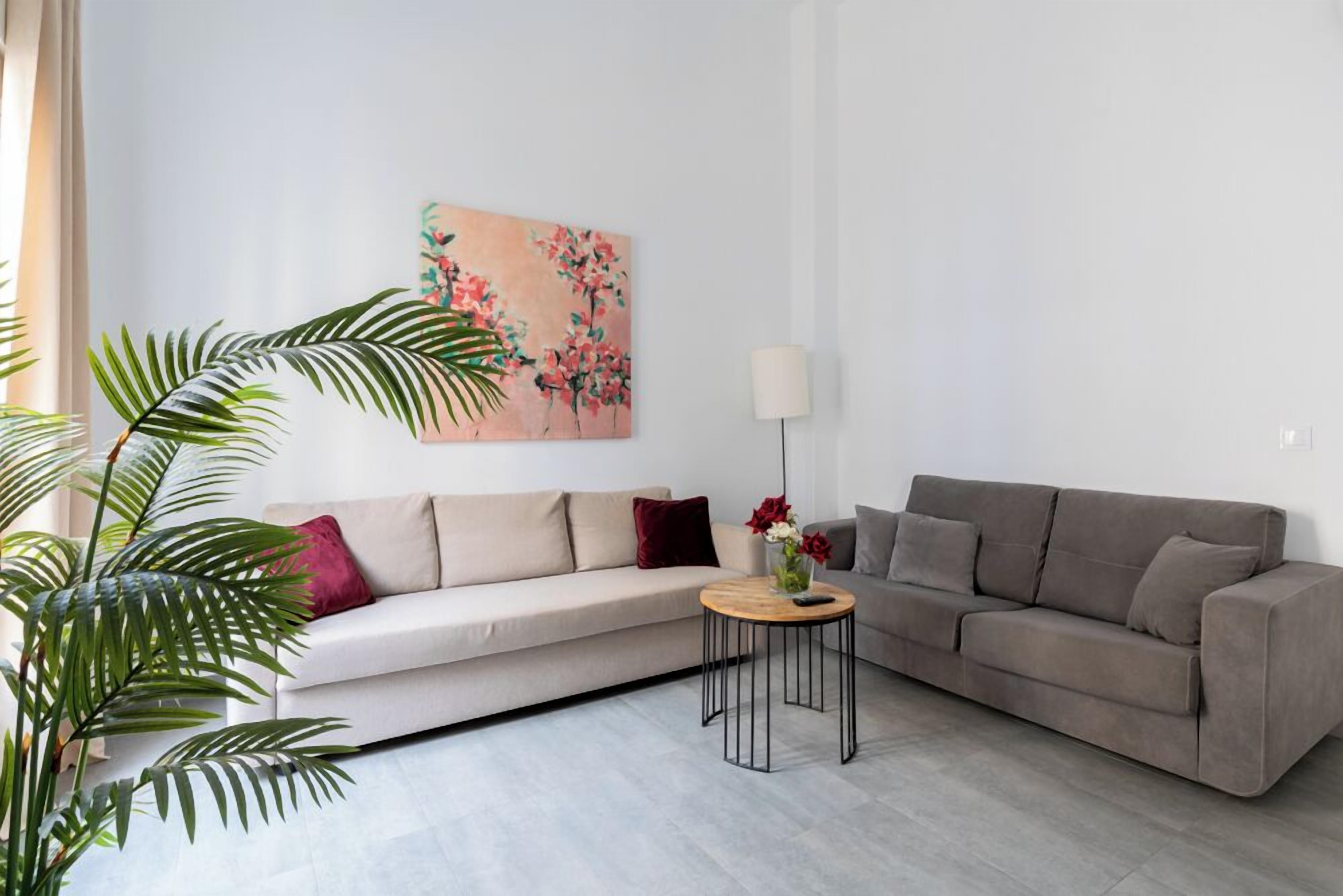 Un salon moderne avec un canapé beige, un canapé gris, une petite table ronde ornée d’un vase de fleurs et un grand tableau accroché au mur.