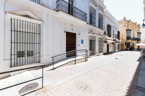 Une ruelle étroite pavée, bordée de bâtiments historiques, où l’on aperçoit un immeuble blanc doté d’une balustrade en métal et d’une porte portant le numéro 4.