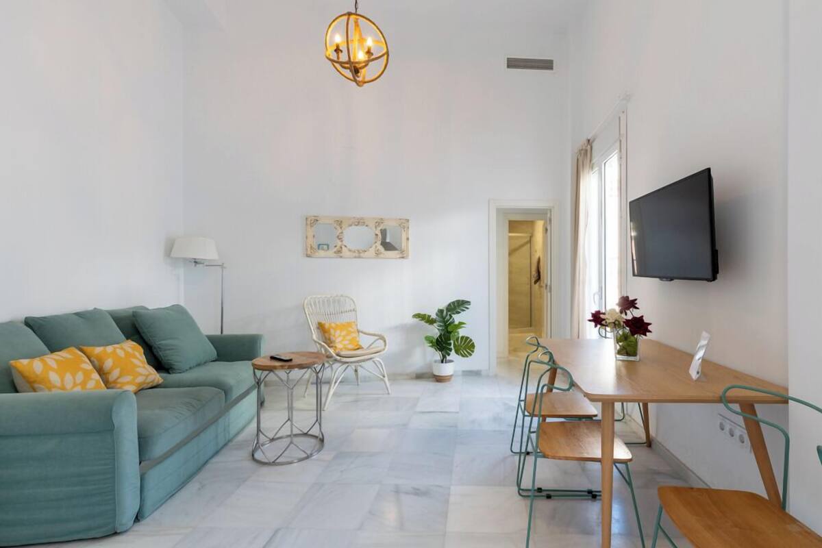 A modern living room with a sofa, a dining table, chairs, a TV, a lamp, and a potted plant.