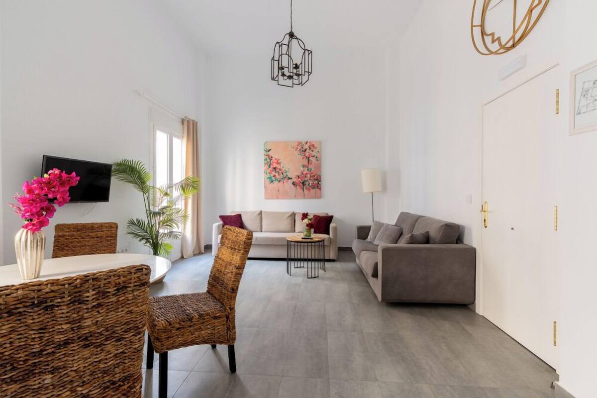 A modern living room with a sofa, a dining table with chairs, a TV, and a painting on the wall.