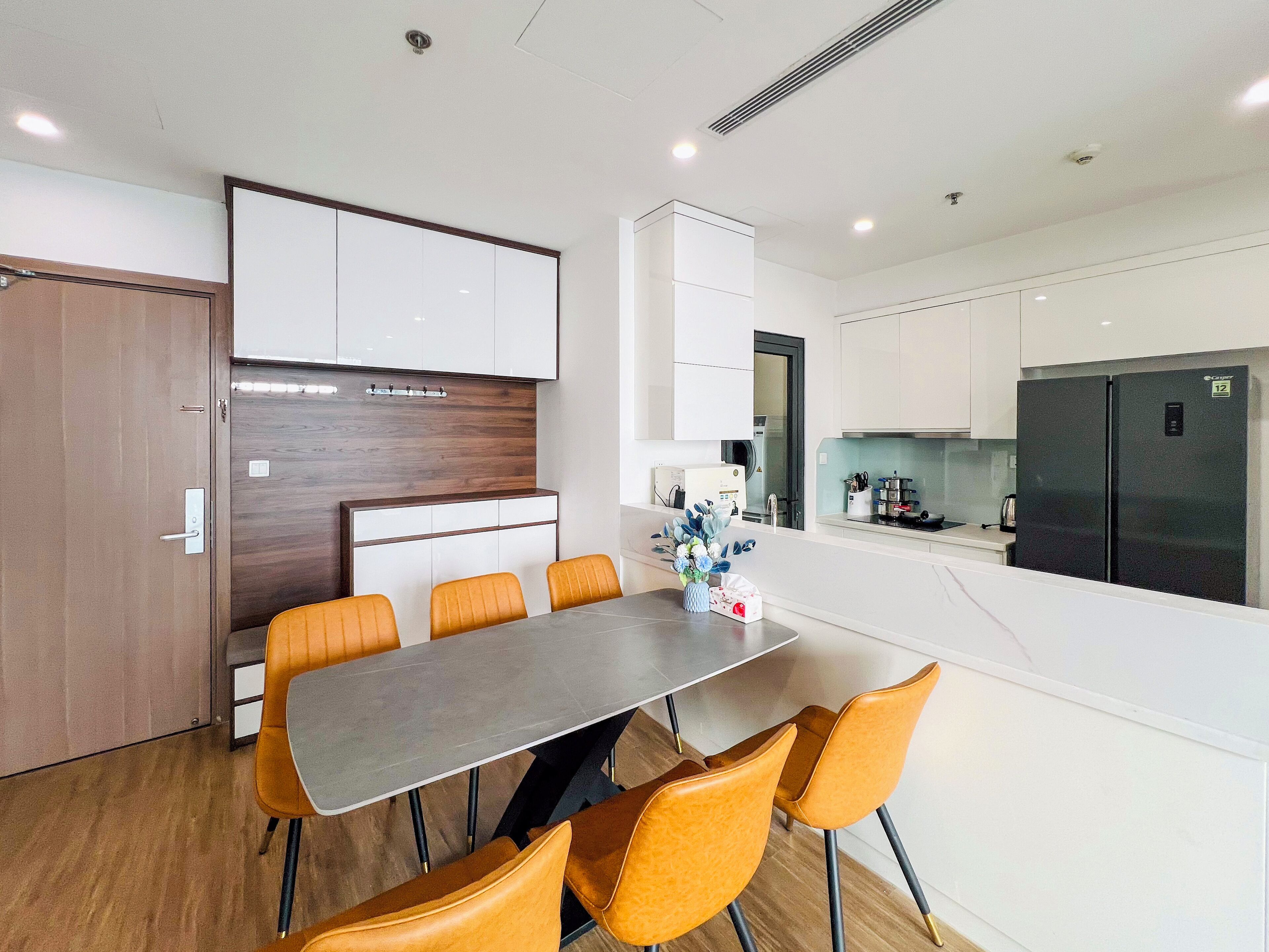 Eine moderne Küche mit weißen Schränken, einem schwarzen Kühlschrank und einem Essbereich mit Tisch und orangefarbenen Stühlen.