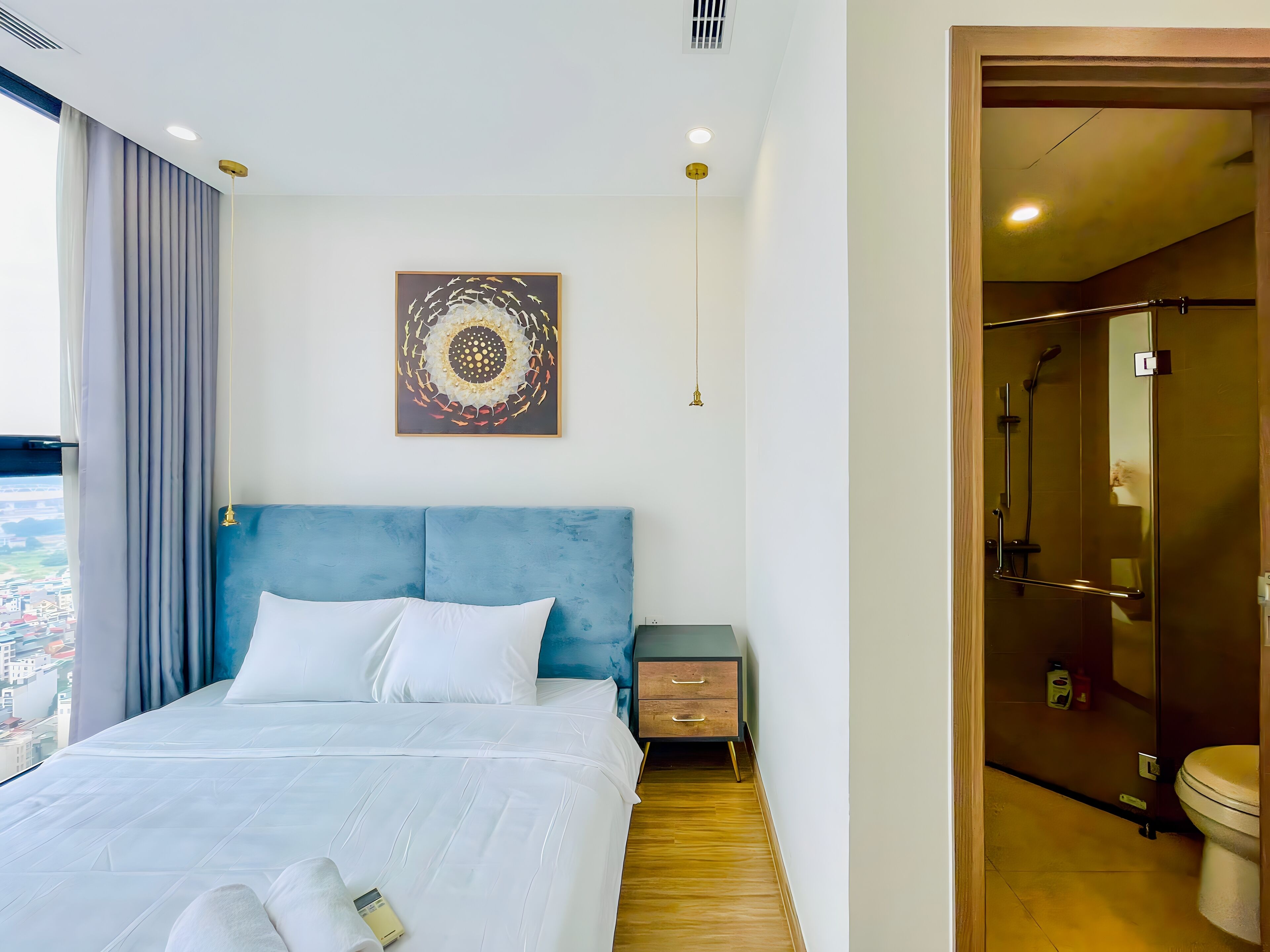 Habitación de hotel moderna con una cama grande, una mesita de noche, una obra de arte en la pared y vista a la ciudad.