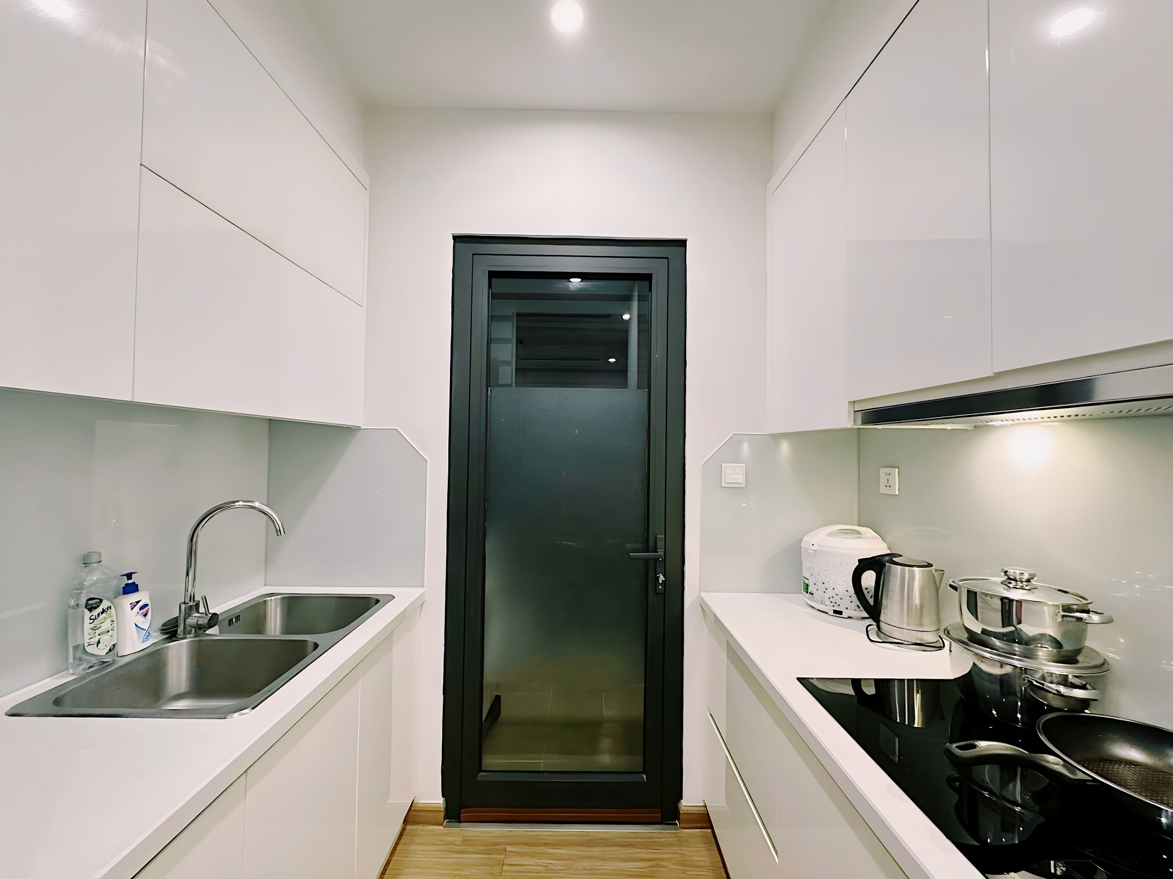 Una cocina compacta con armarios blancos, un lavamanos de acero inoxidable, una puerta negra y una estufa.