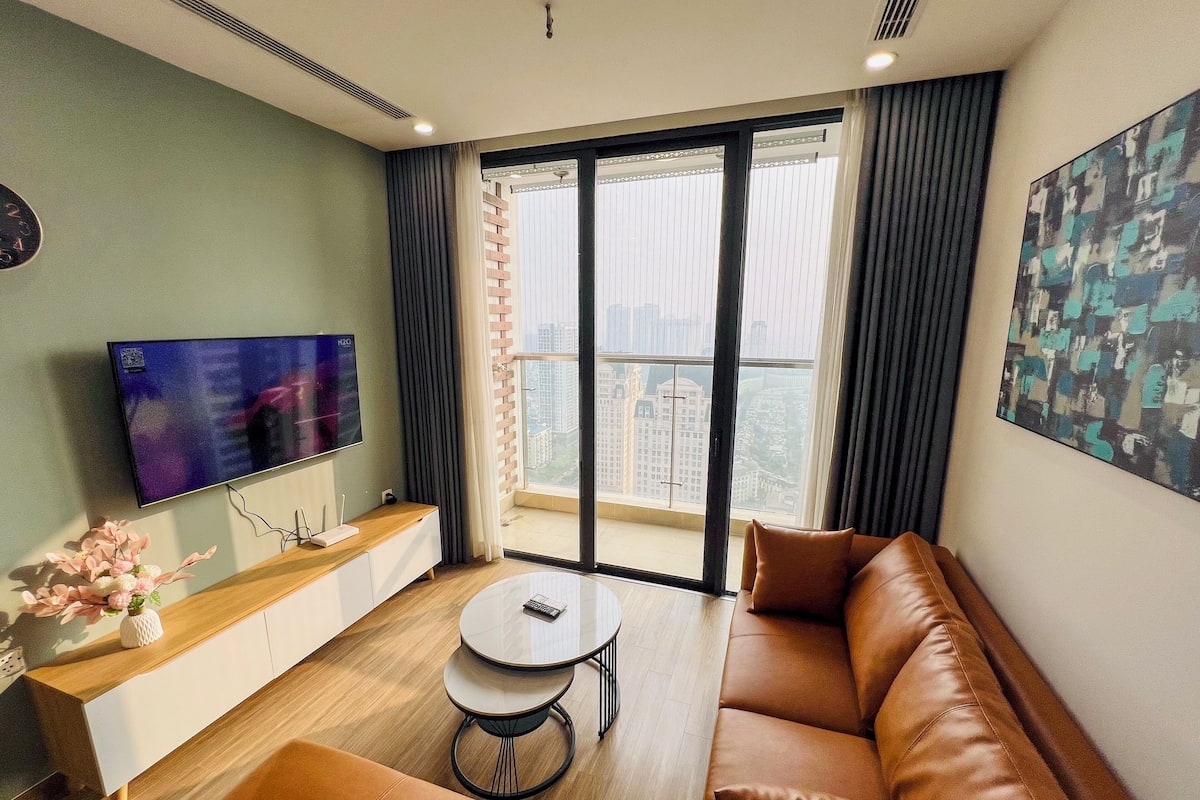 Un salon moderne avec un canapé, une table basse, un téléviseur et un balcon offrant une vue sur la ville.