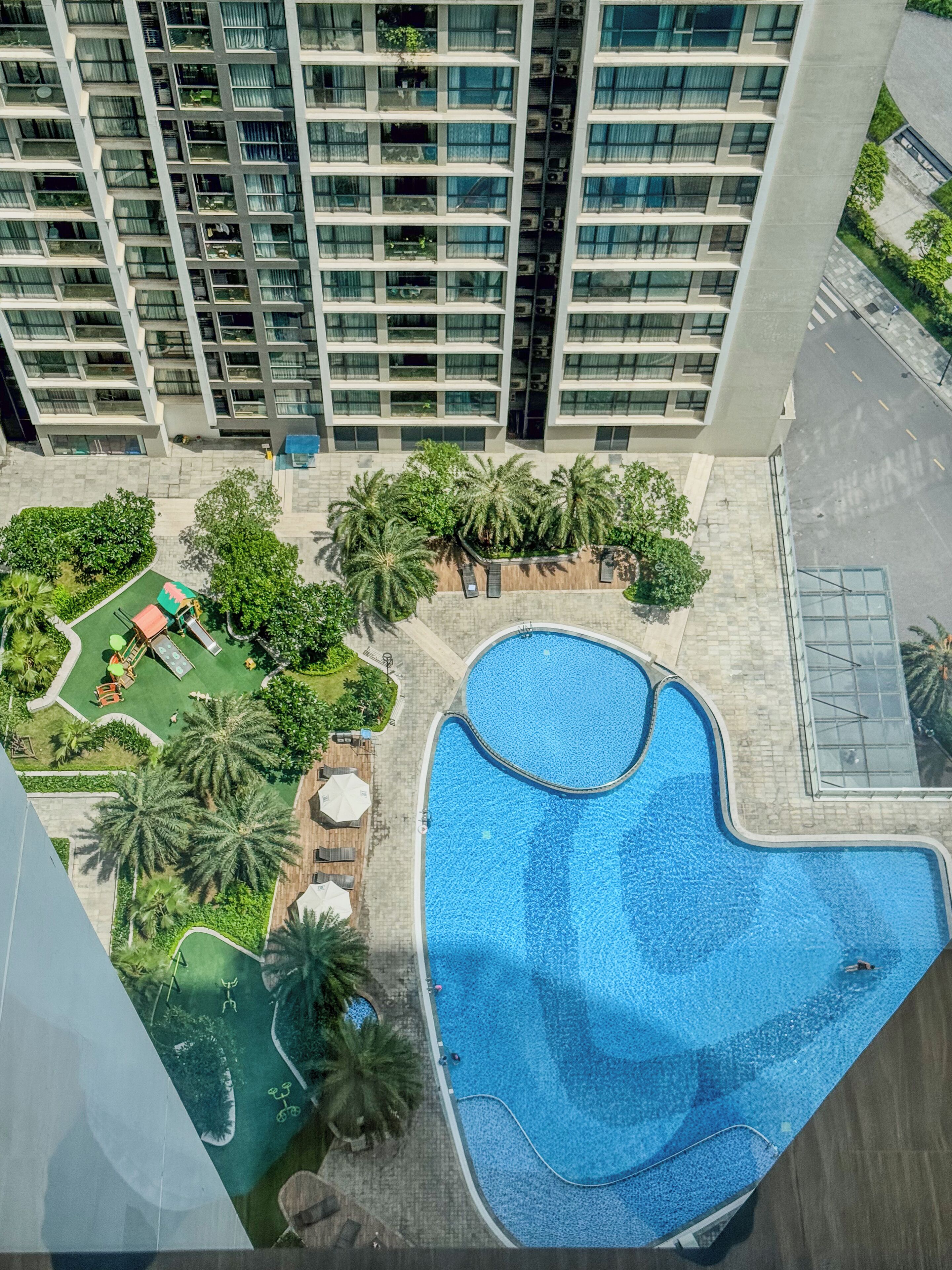 A high-rise building with a rooftop pool surrounded by palm trees and a children's play area.