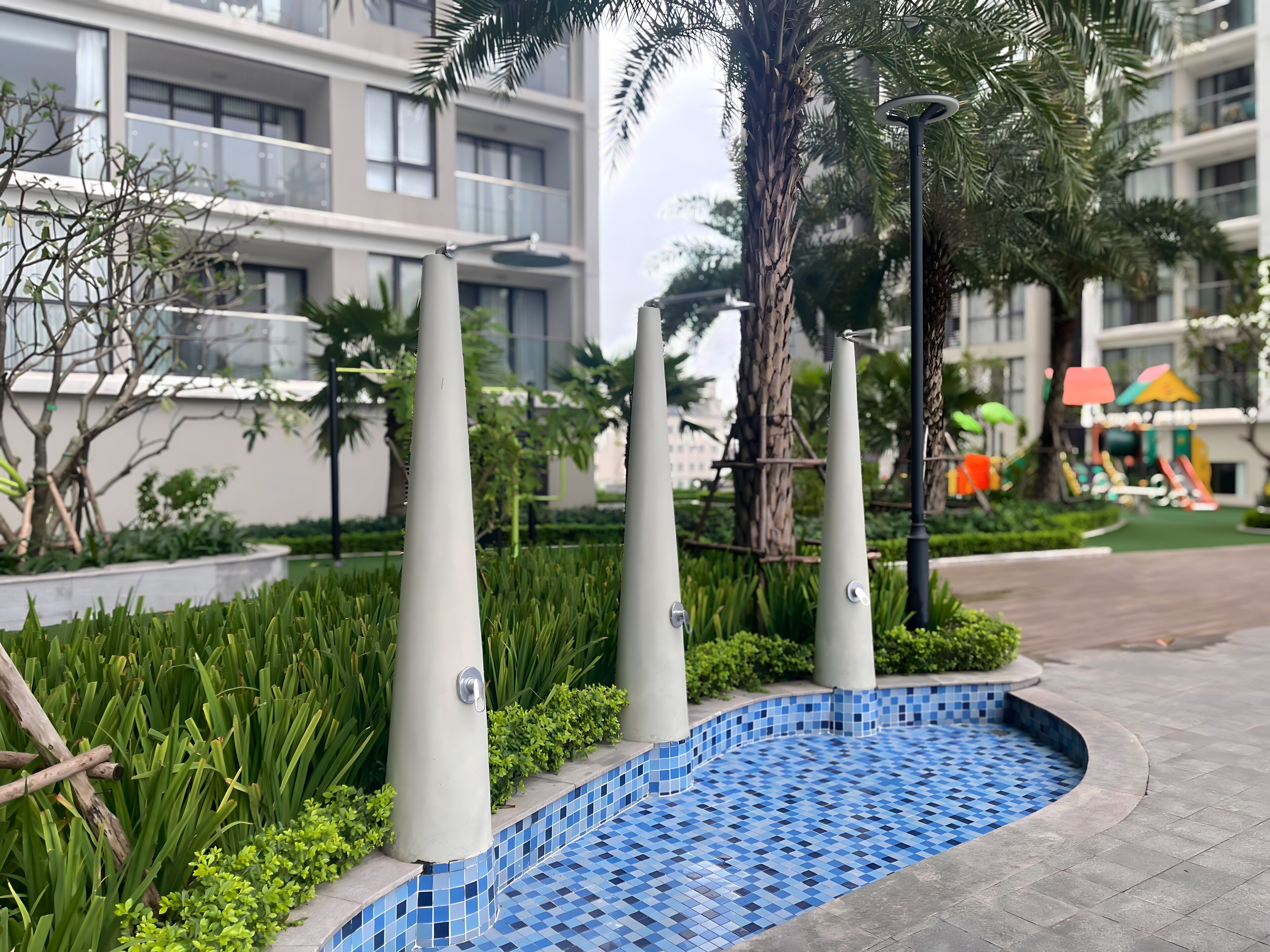 A modern building with a pool area, surrounded by greenery and palm trees.