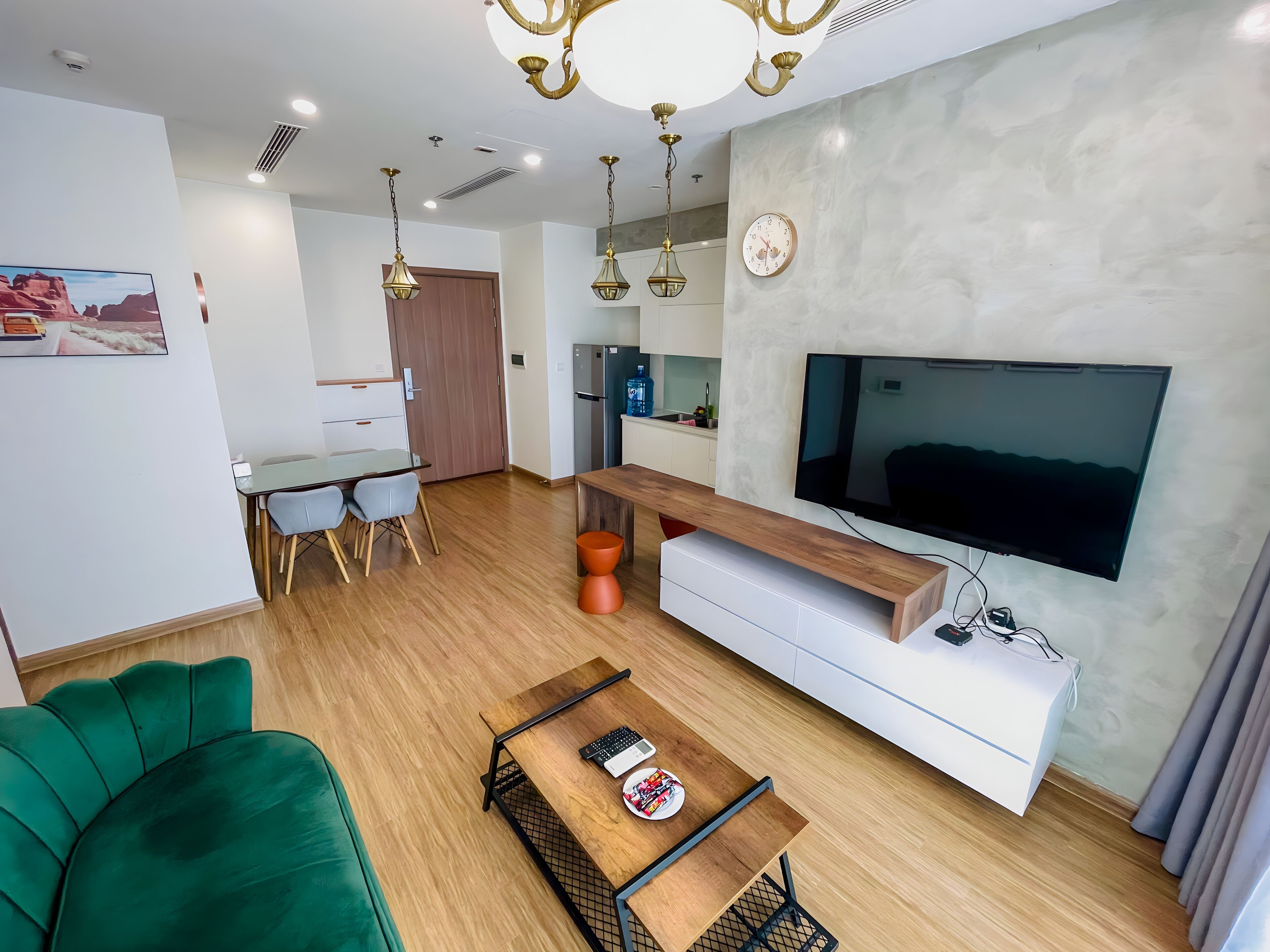 Ein modernes Wohnzimmer mit einem Flachbildfernseher, einem Couchtisch aus Holz, einem grünen Sofa und einem Essbereich mit Tisch und Stühlen.