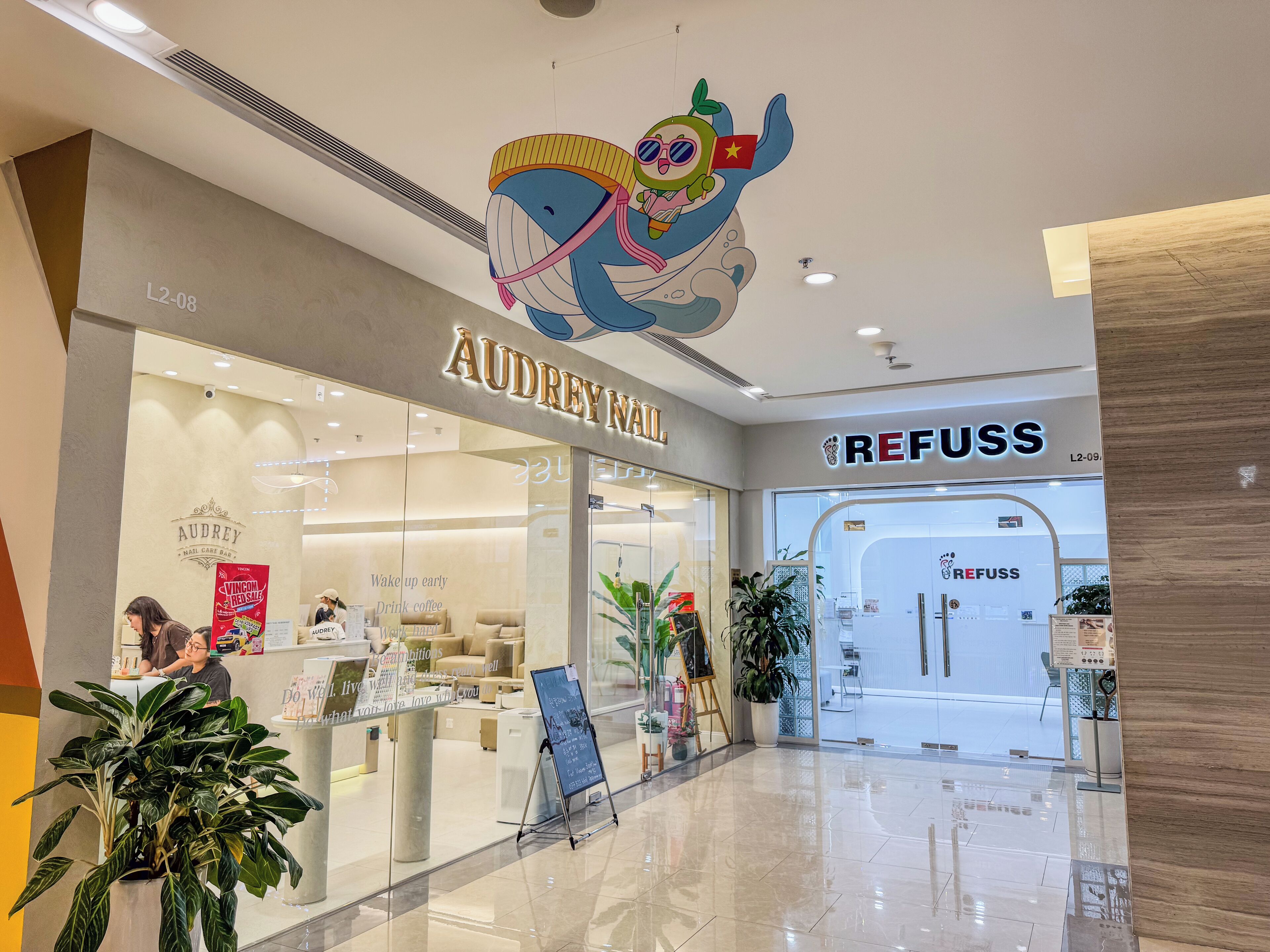 A shopping mall interior with stores 'AUDREY NAIL' and 'REFUSS'.