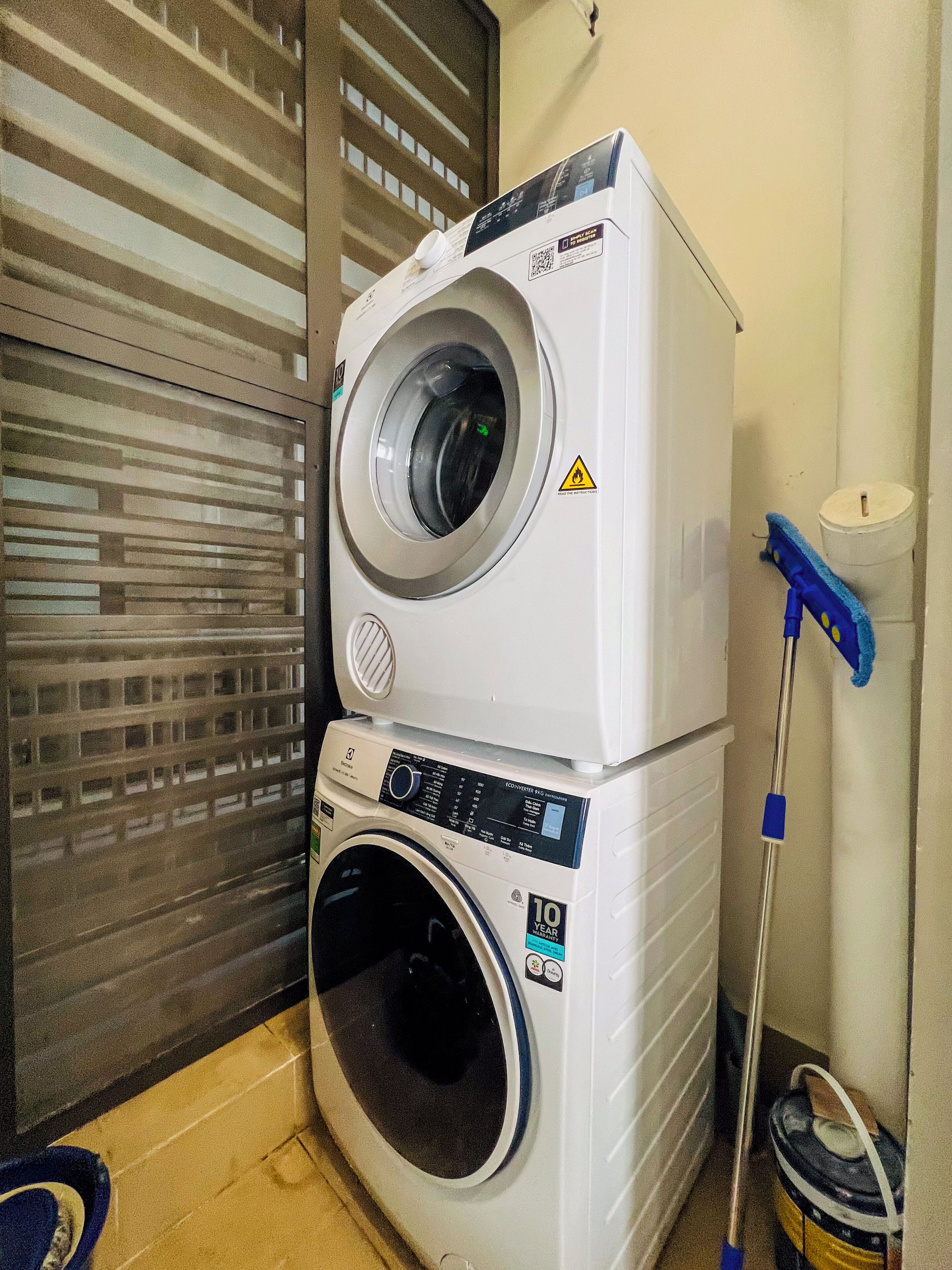 Máquina de lavar e secar empilhadas em uma lavanderia, com um esfregão e balde por perto.