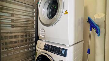 Máquina de lavar e secar empilhadas em uma lavanderia, com um esfregão e balde por perto.