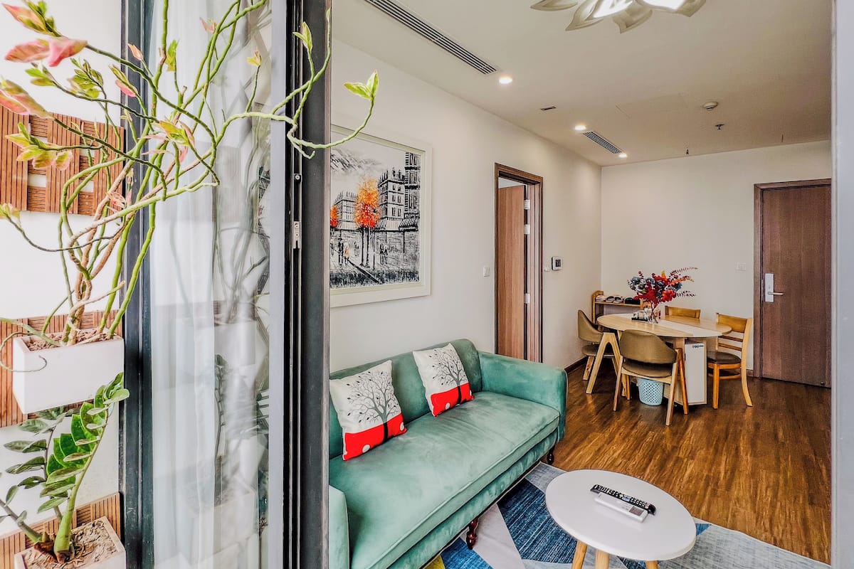 Un salon moderne avec un canapé vert, une table à manger et une grande fenêtre agrémentée de plantes.
