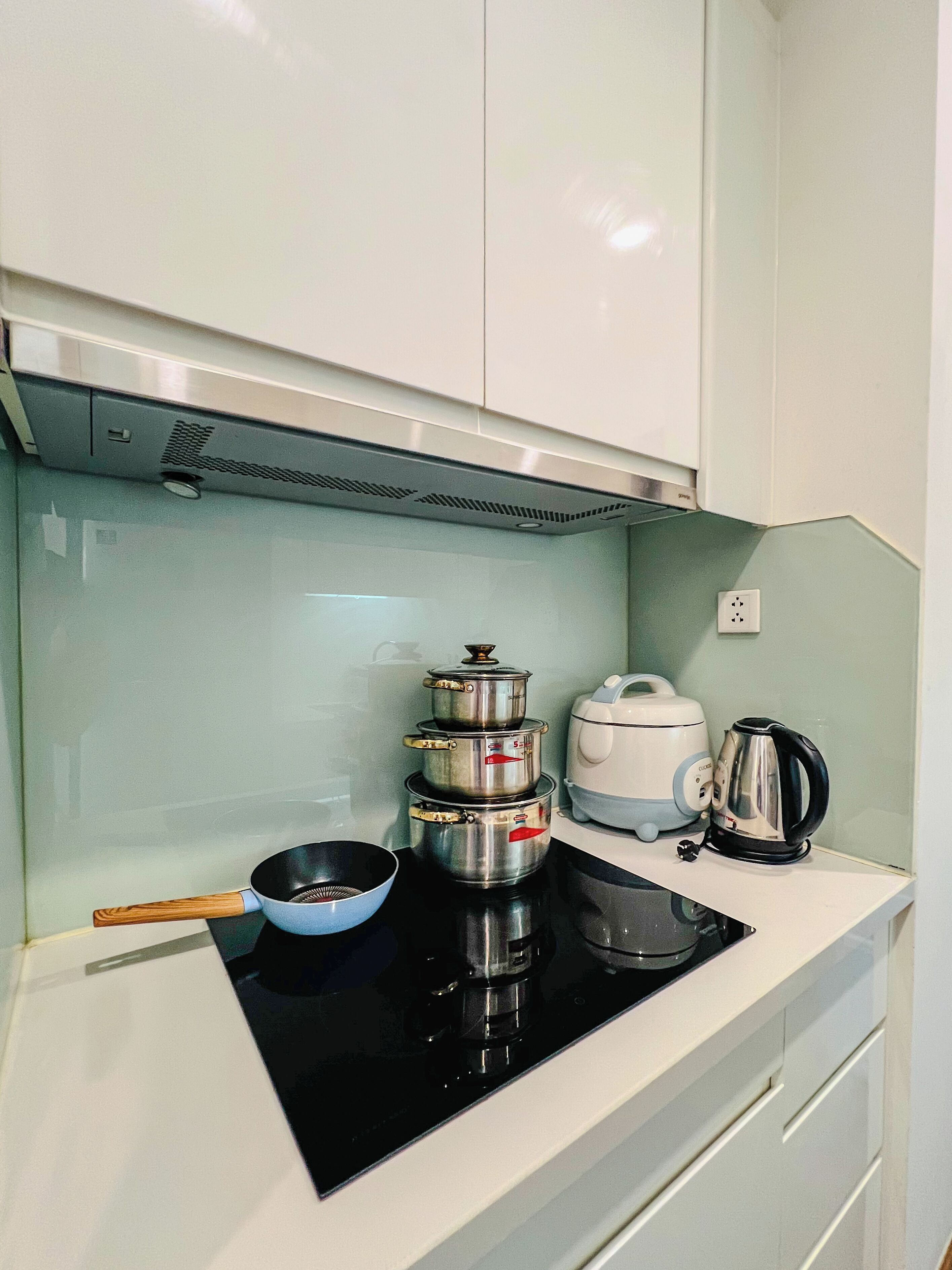 A compact kitchen with a stove, pots, a kettle, and a rice cooker.