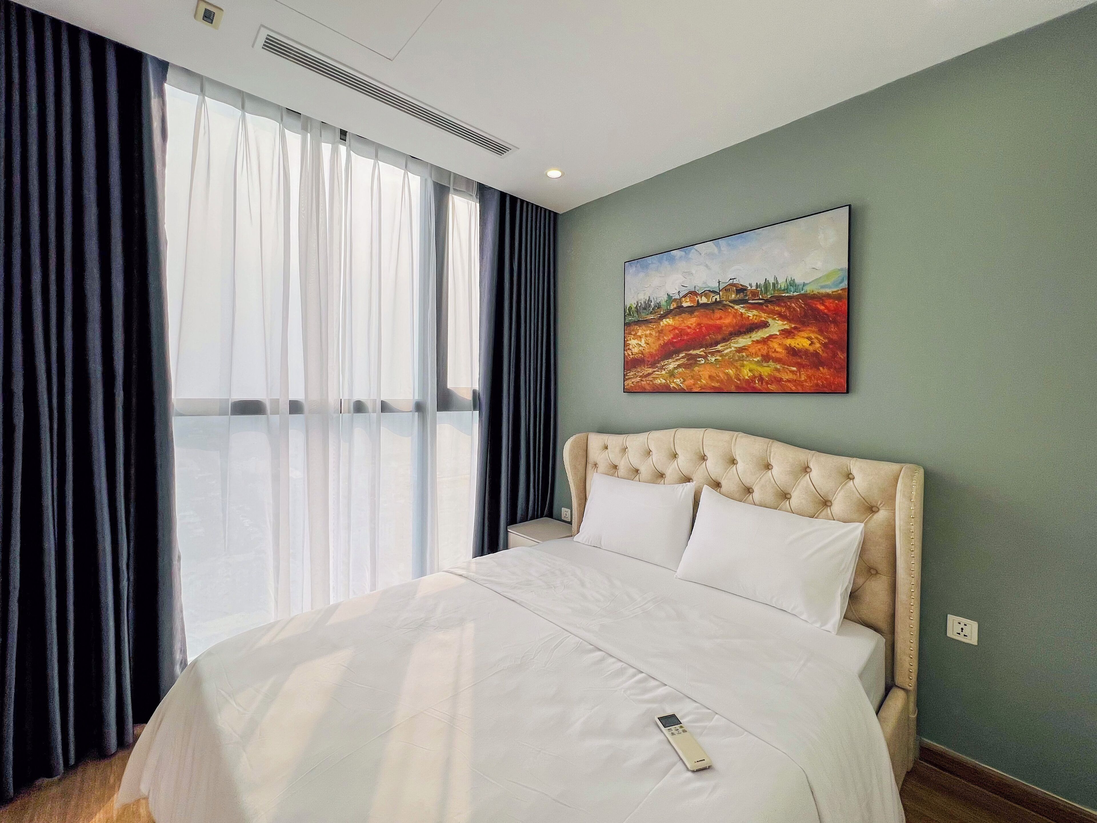 A hotel room with a large bed, a painting on the wall, and a window with curtains.