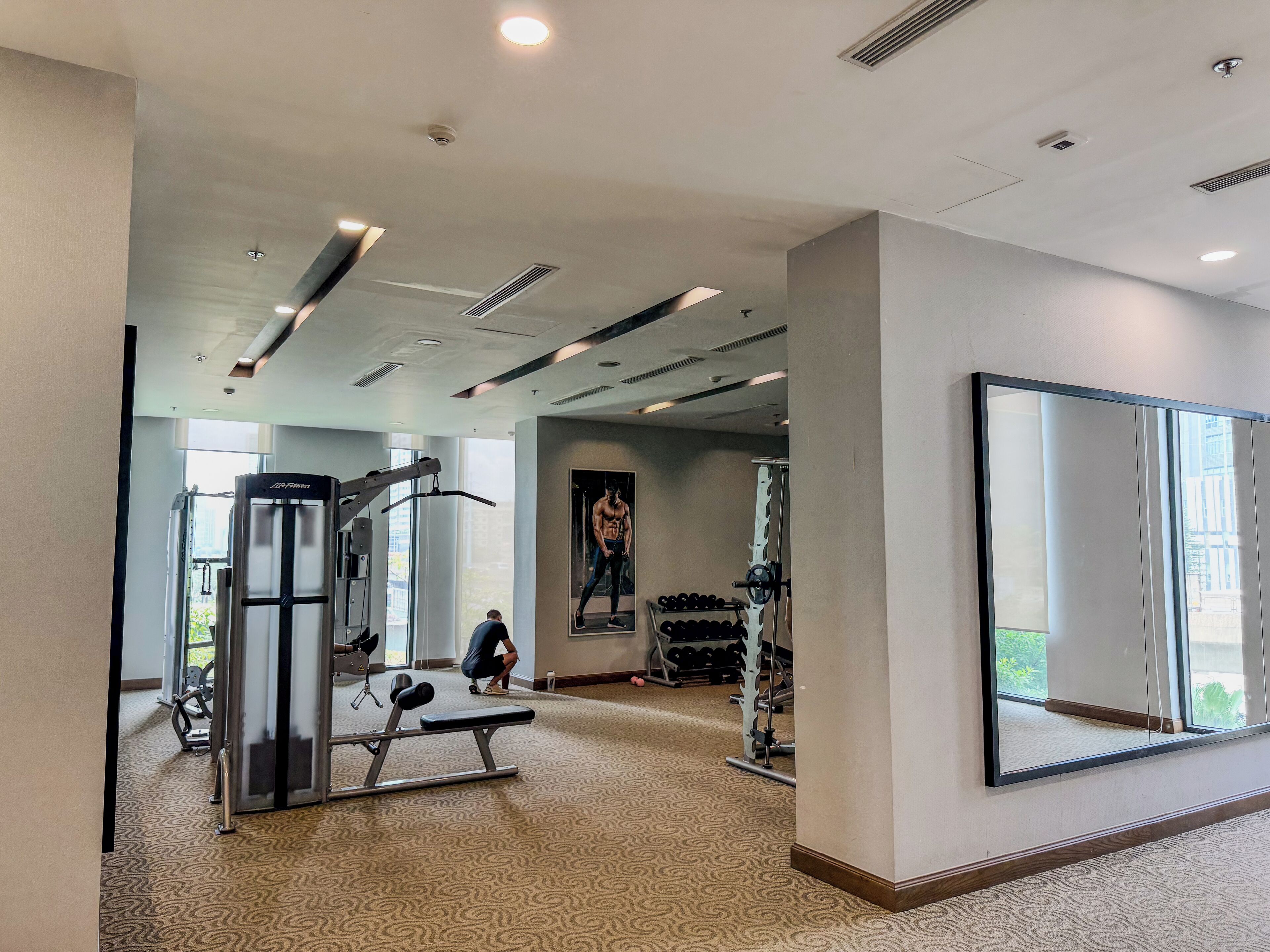 A gym with exercise equipment, a large mirror, and a view of the outdoors through large windows.