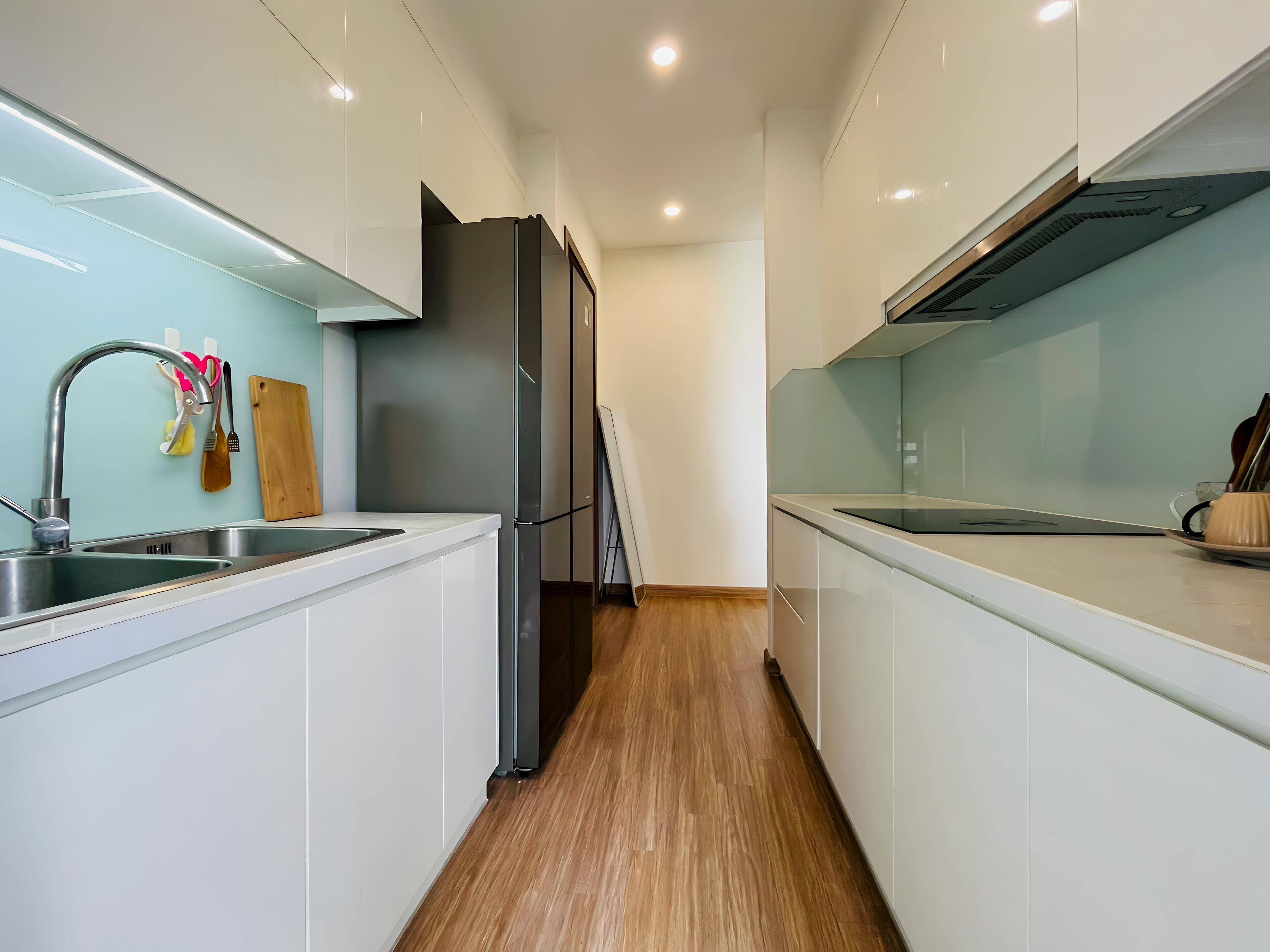A modern kitchen with white cabinets, stainless steel appliances, and wooden flooring.